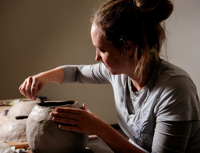 Ceramics student sculpting the top of a clay vase