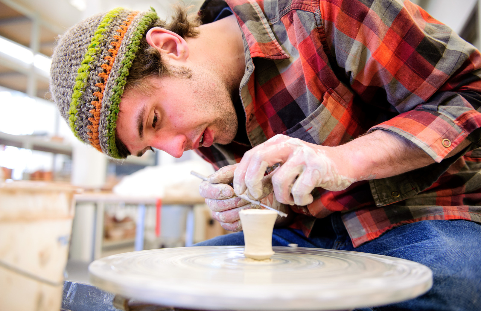 Ceramics student sculpting small clay pot on a pottery wheel
