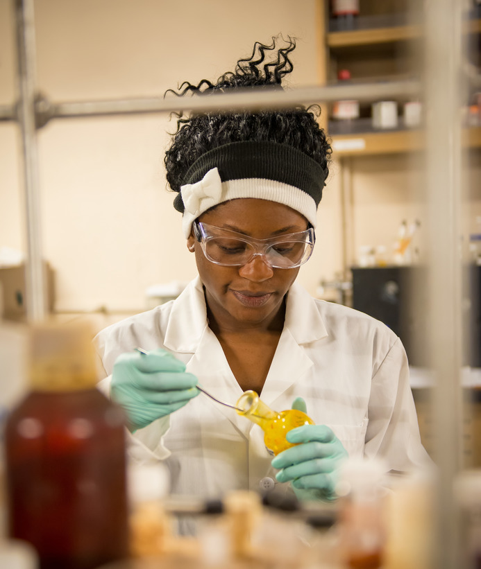 A student wearing a lab coat, gloves and safety goggles uses the equipment in a chemistry lab