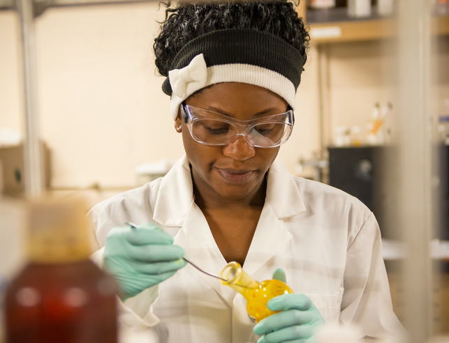 A student wearing a lab coat, gloves and safety goggles uses the equipment in a chemistry lab