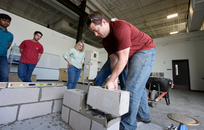 Faculty members and students assembling a wall full of cinder blocks