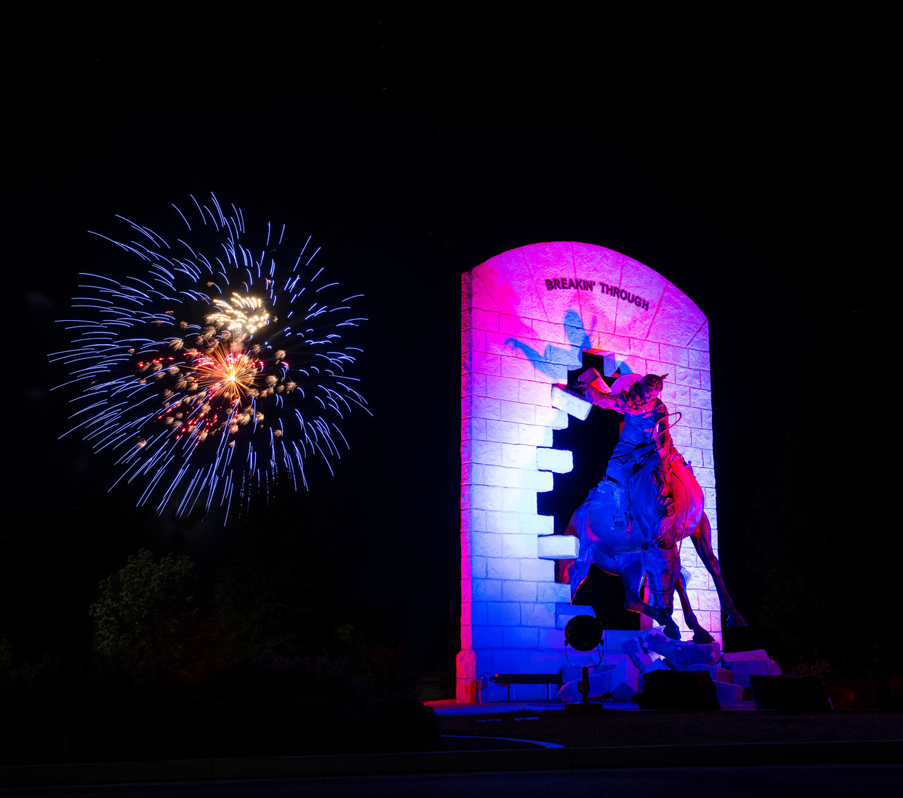 "Breakin' Through" statue at night with fireworks behind it