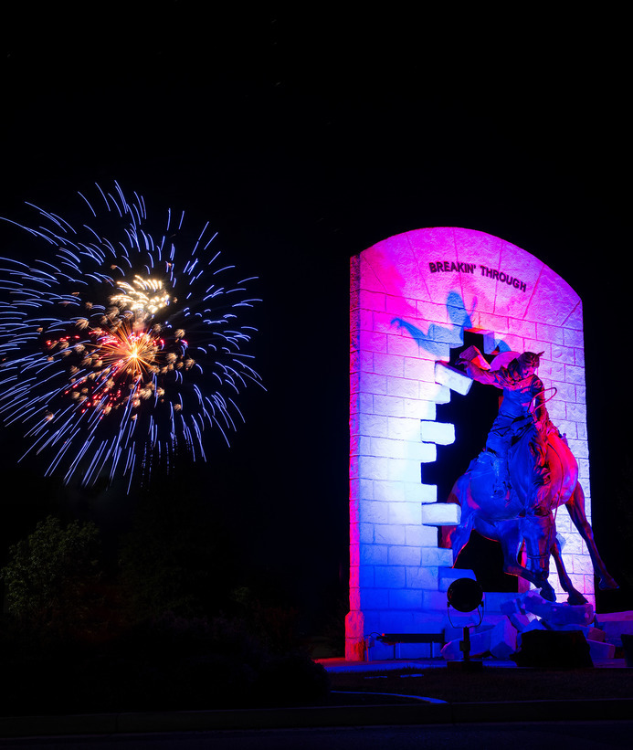 "Breakin' Through" statue at night with fireworks behind it