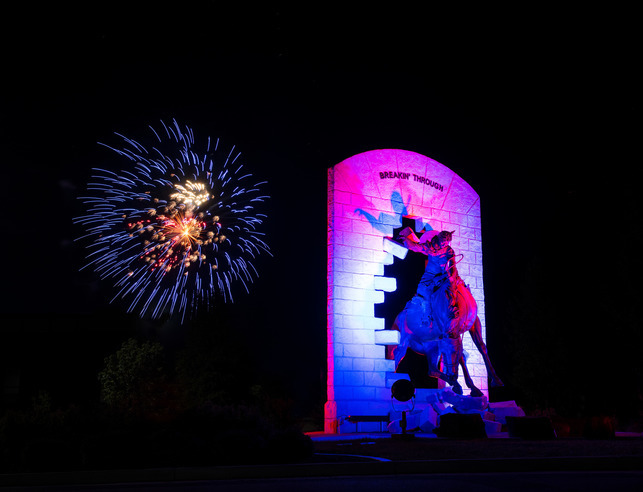 "Breakin' Through" statue at night with fireworks behind it