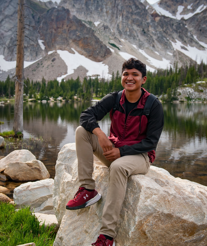 Student smiles at the camera in front of a mountain lake