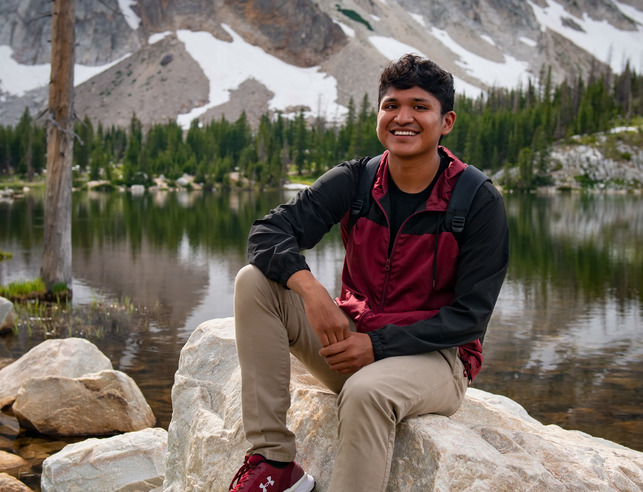 Student smiles at the camera in front of a mountain lake