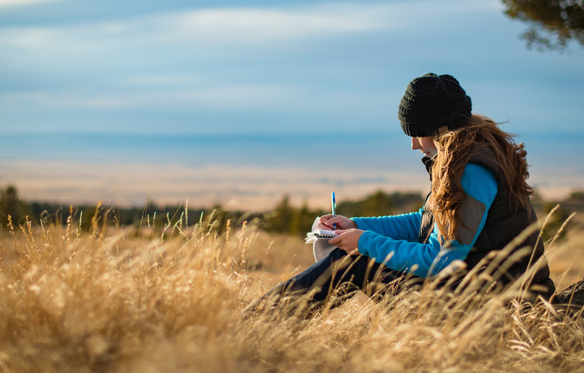 A student writes thoughtfully outside with a scenic landsape