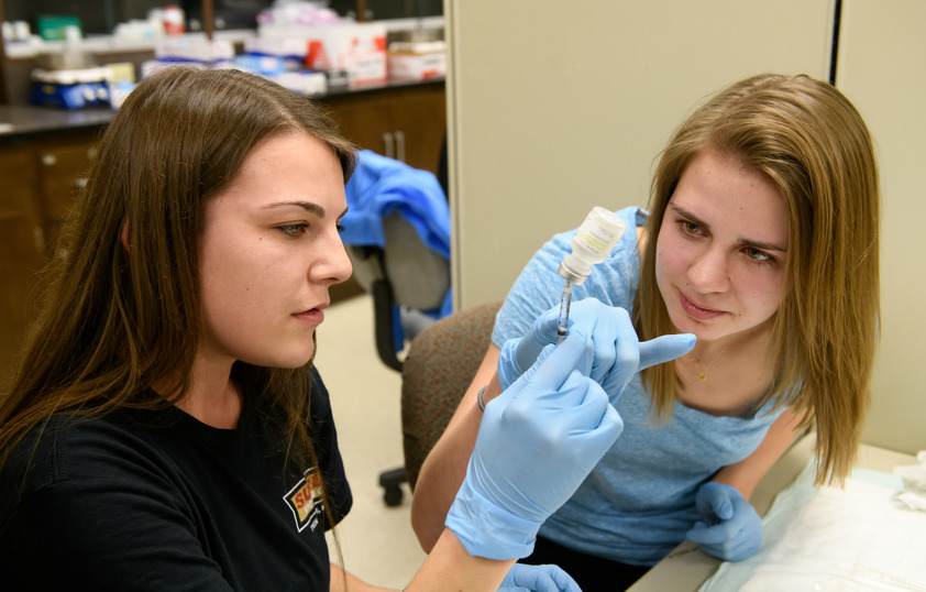 Two students practice with a syringe and vile