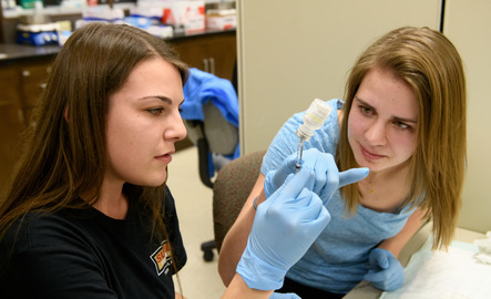 Two dental hygiene students practice with a syringe and vile