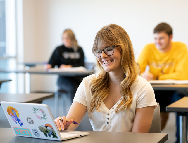 Student smiling at laptop in class