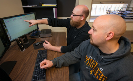 Two people sit and look at computer screens with a graph on it together
