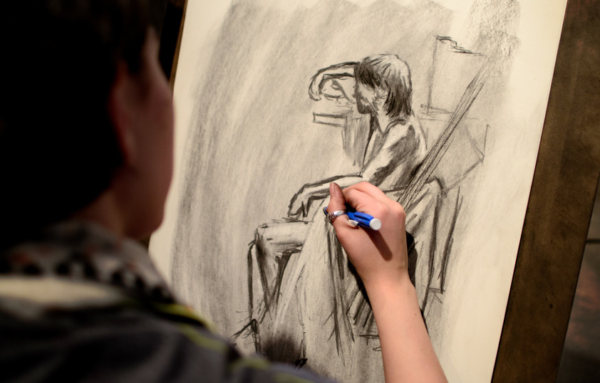 A student sketching a person with a pencil on a white canvas