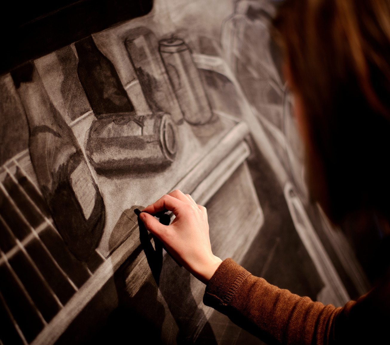 A student sketching various cans and bottles on a canvas