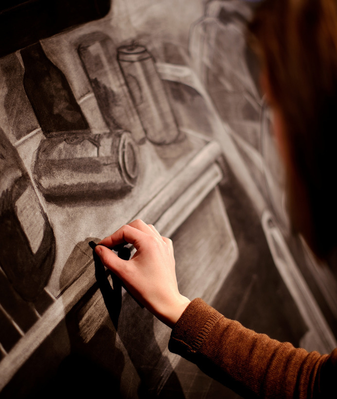A student sketching various cans and bottles on a canvas