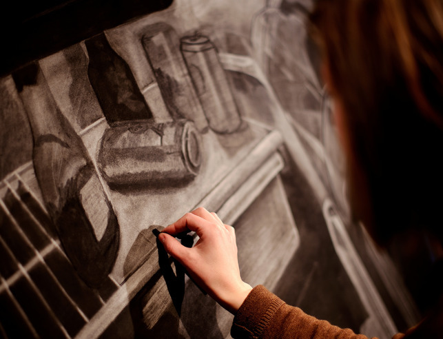 A student sketching various cans and bottles on a canvas