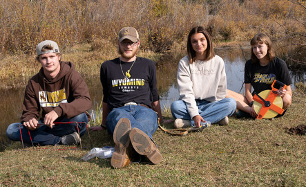 Four ecology students smile for a picture next to a body of water during class