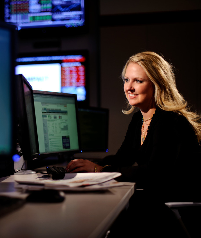 An economist looks at two computer screens while smiling