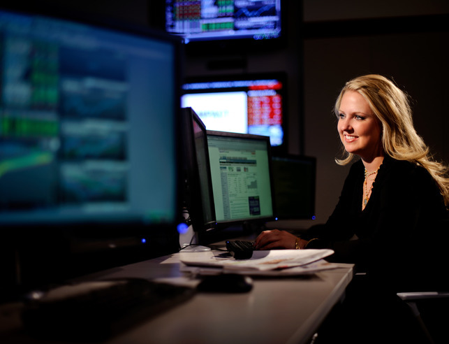 An economist looks at two computer screens while smiling