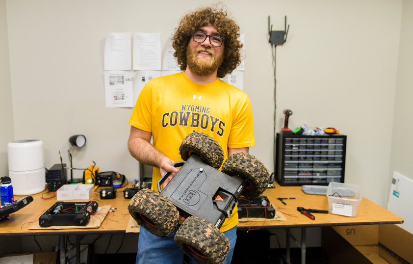 A student smiles for a photo while holding their car robot