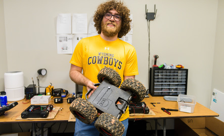 A student smiles while holding their car robot