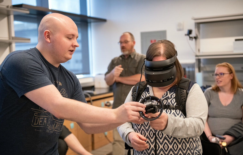 A makerspace worker helps a participant into a VR headset