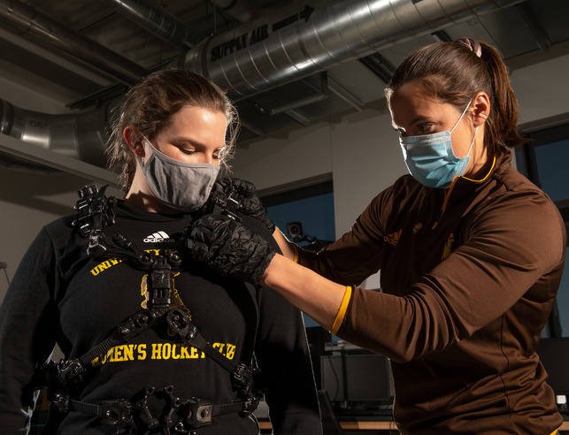 An electrical engineer assists an athlete into an electrical body suit