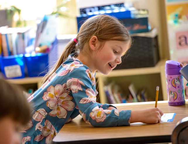 An elementary aged student writes at her desk