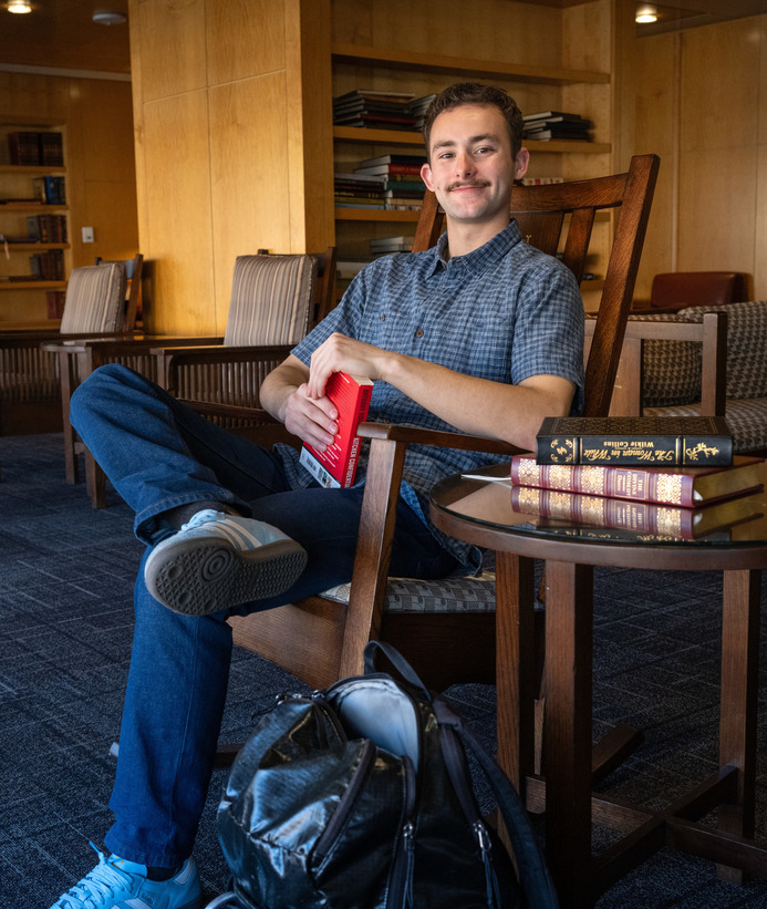 A student smiles while sitting in a rocking chair while holding a book