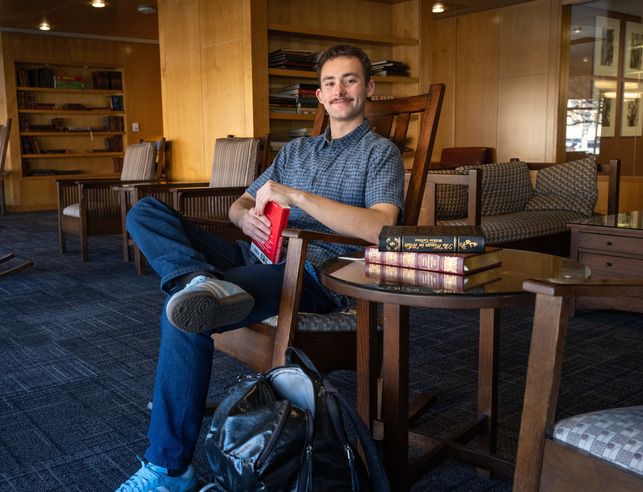 A student smiles while sitting in a rocking chair while holding a book