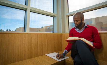 A student writes in a notebook while holding a book open