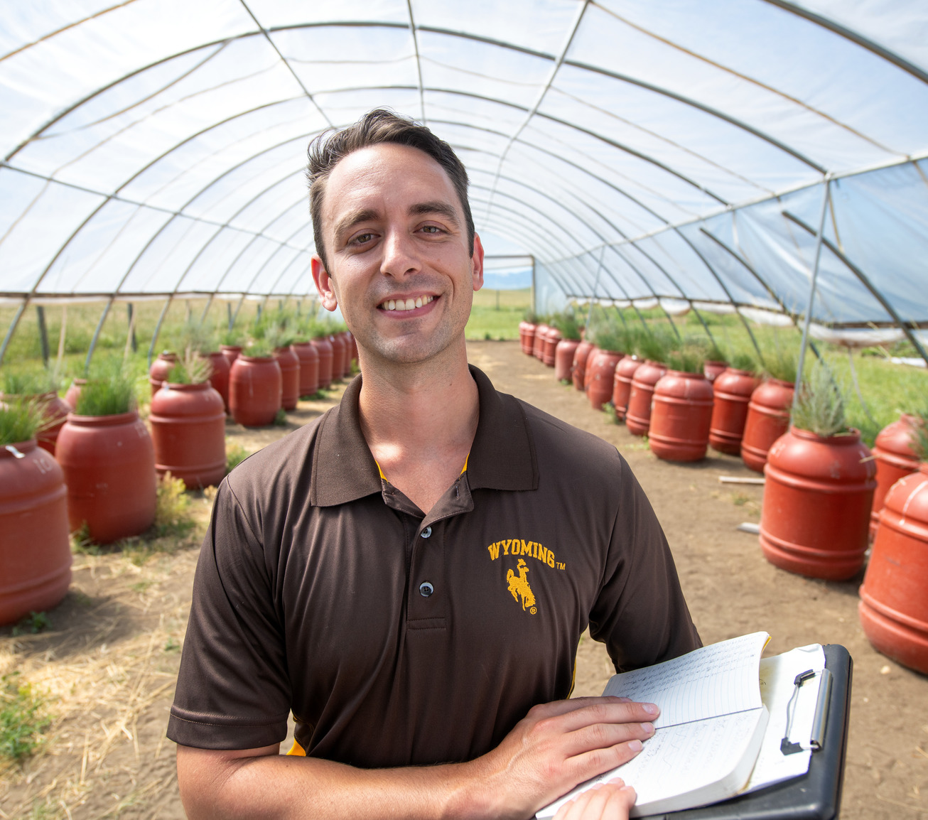 A person stands in front of barrels full of plants with a clip board in his hands