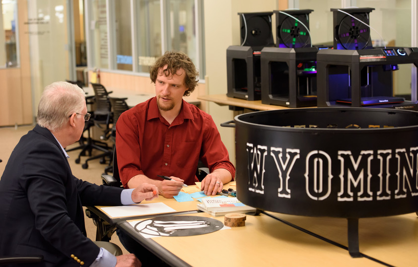 A students sits by a professor with a sign