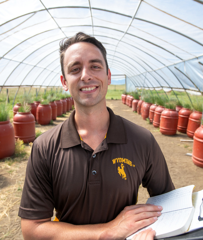 A person stands in front of barrels full of plants with a clip board in his hands