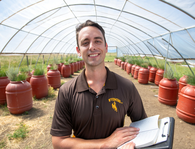 A person stands in front of barrels full of plants with a clip board in his hands