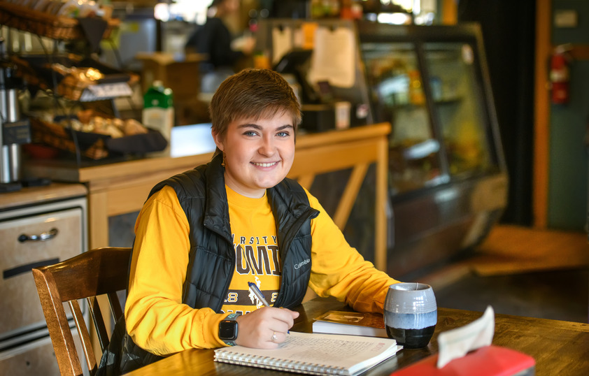A student smiles for the camera while studying in a coffee shop