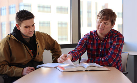 A professor and student look at a textbook together