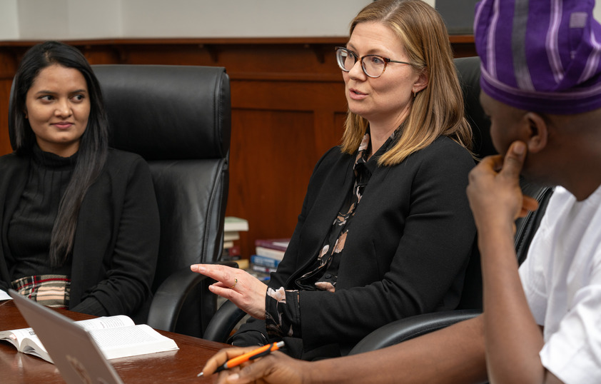 A professor speaks to a group of students at a conference table