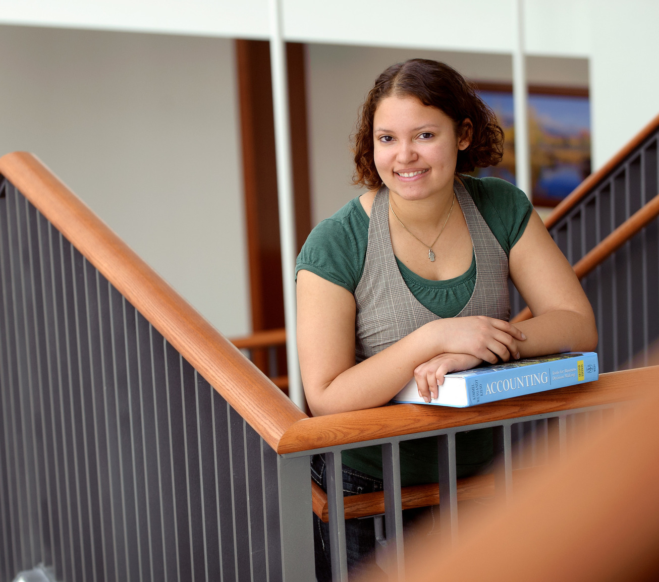 A student holds a book in a stairwell looking at the camera