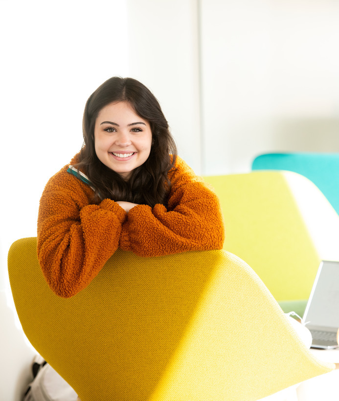 A student smiles for a photo while sitting in a chair