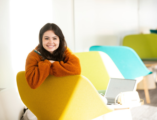 A student smiles for a photo while sitting in a chair