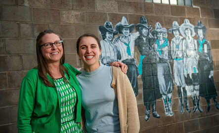 Two people standing in front of a mural on a brick wall