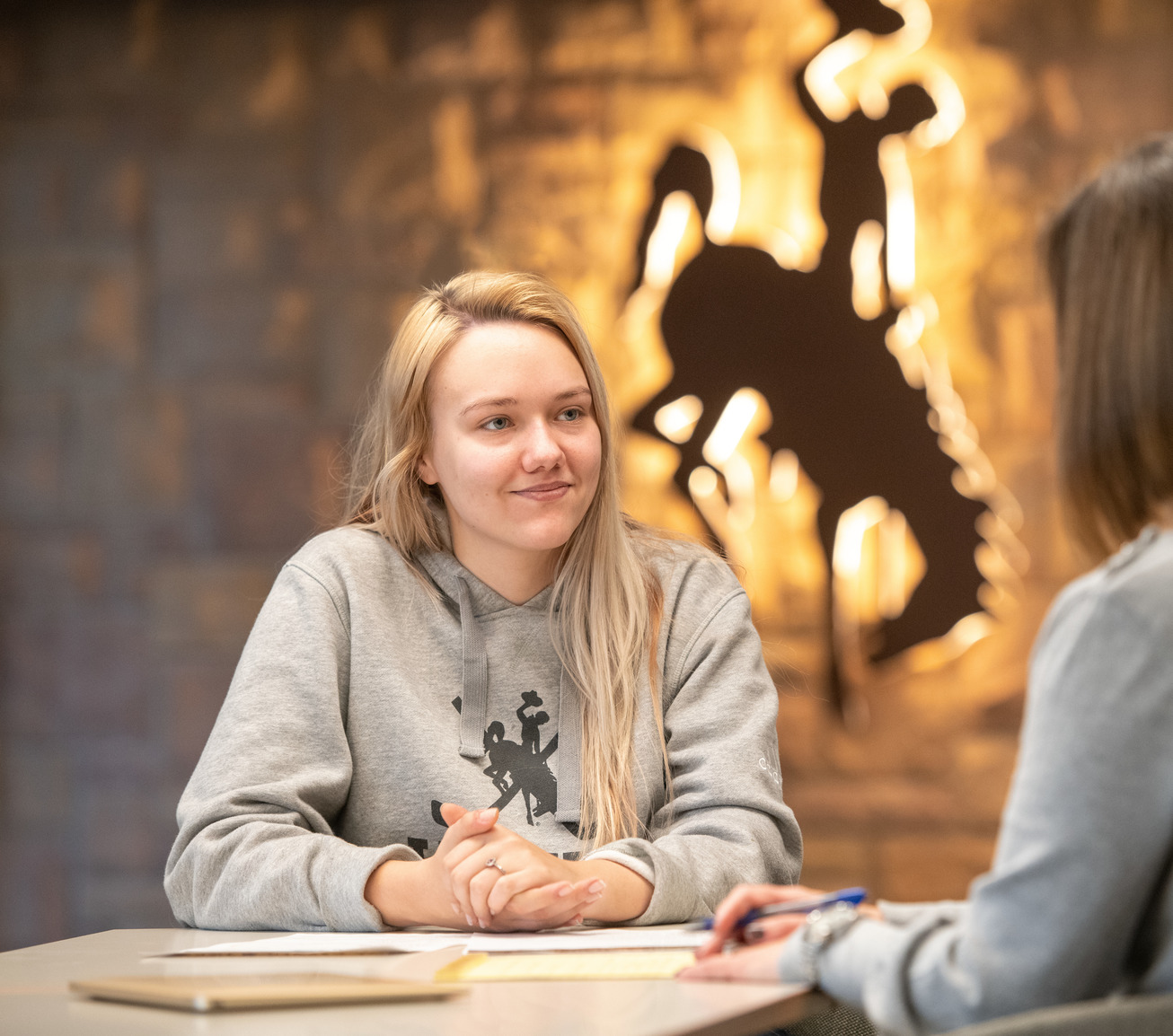 A student sits in front of a backlit UW Steamboat horse icon logo.