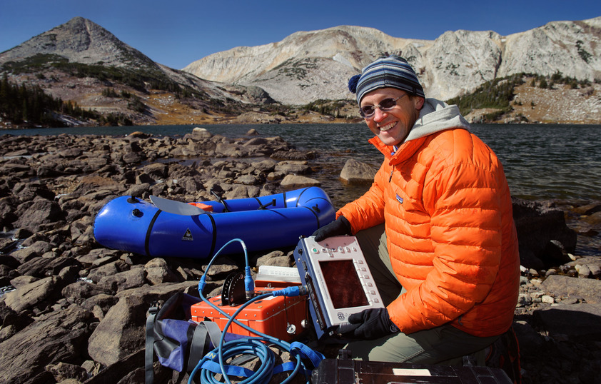 A graduate student works with geographic equipment by a lake.
