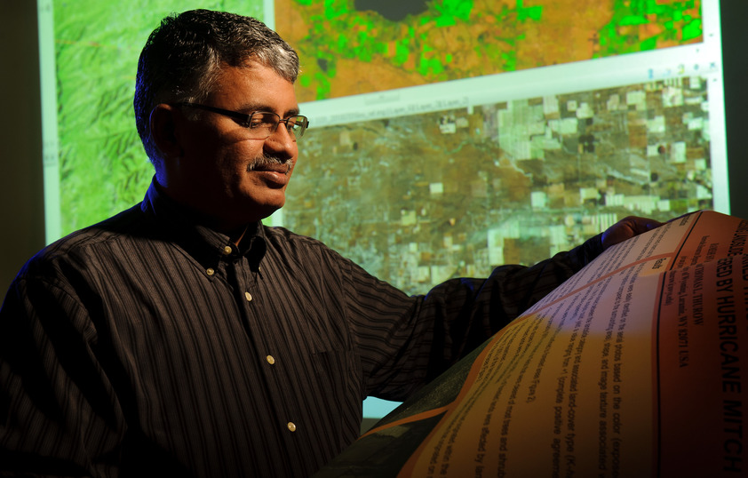 A professor looks at a globe with a green map behind him