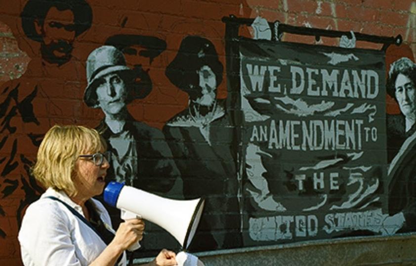 Professor giving speech in front of mural