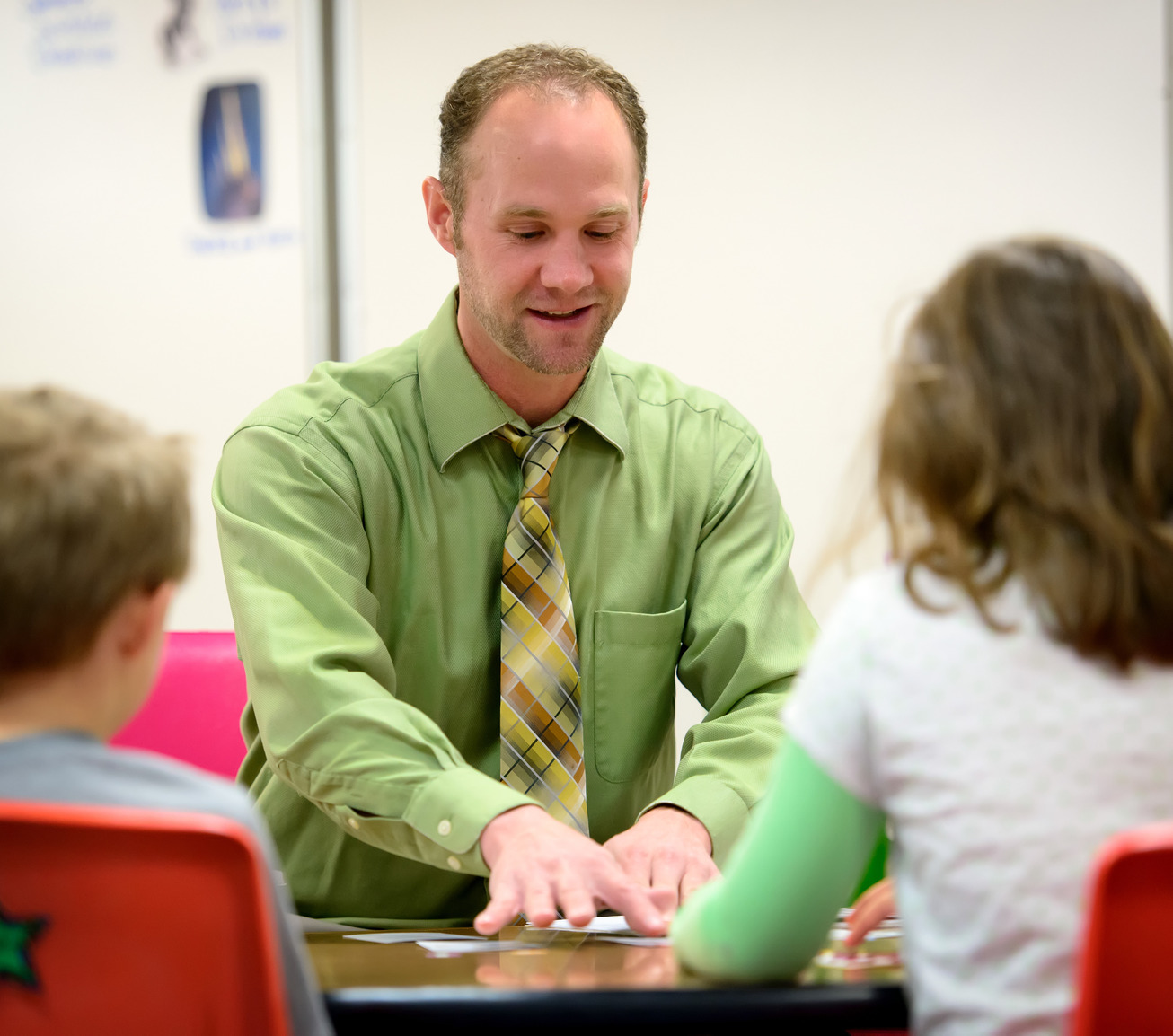 Teacher sits at table with two students and shows them different cards