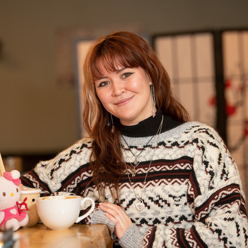 A student softly smiles for a photo while holding a coffee cup