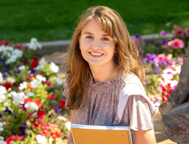 A student smiles for a photo while holding a notebook