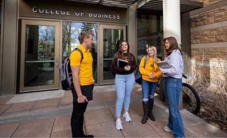 A group of students stand and talk outside of the College of Business