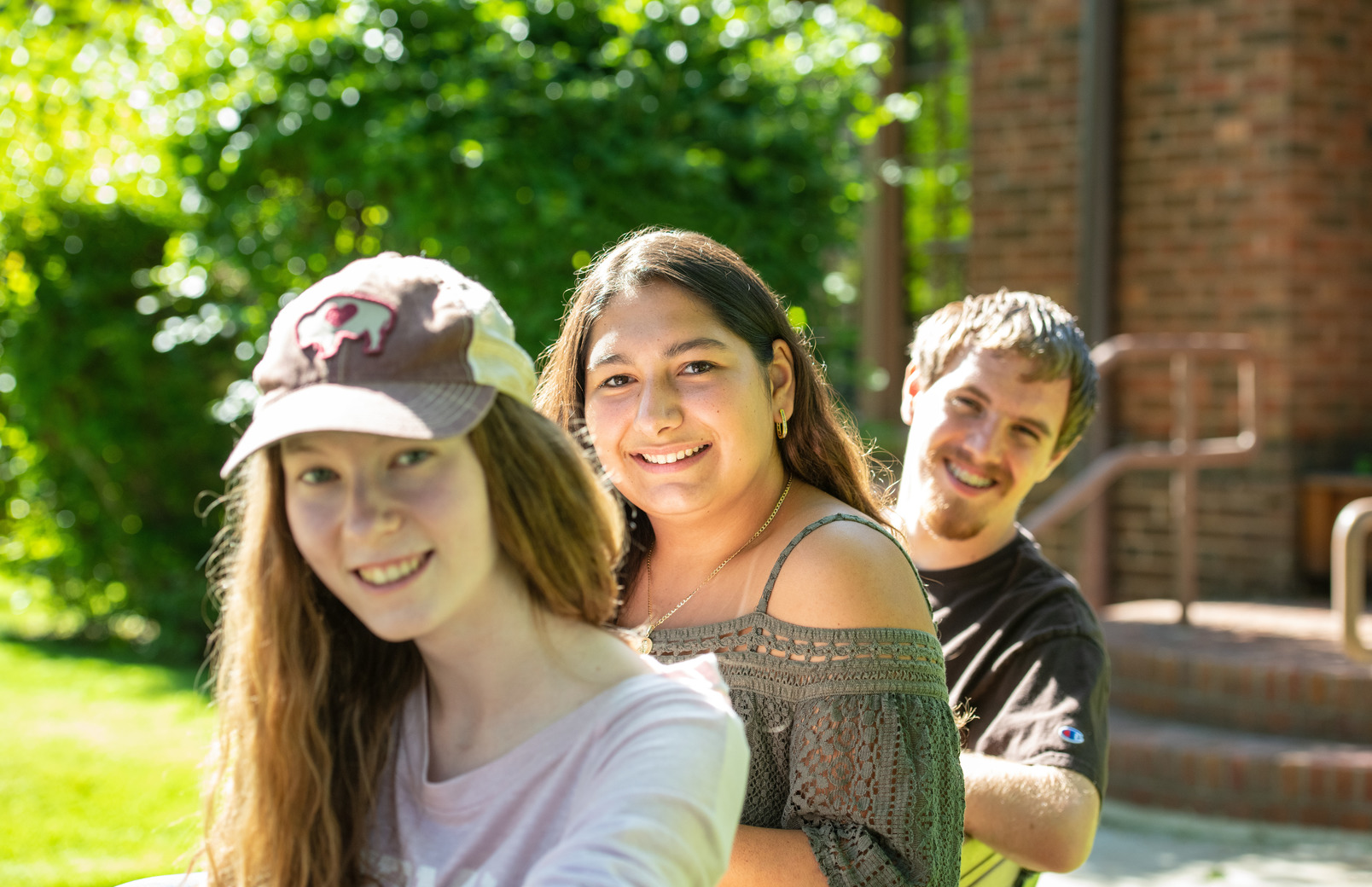 Three students sitting on bench and smiling for photo